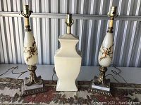 Three vintage table lamps shown on a decorative table cloth, two with floral designs and one plain