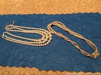 Two vintage costume jewelry necklaces laid out on a blue fabric. One is a multi-strand faux pearl necklace and the other is a single strand faux pearl necklace.