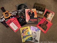 Display of all items in the collection arranged on carpet floor, showing books, DVD, toy guitar, and sports programs.