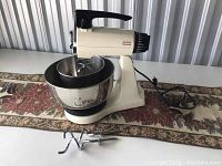 Side view of the Sunbeam Mixmaster with bowl and dough hooks on a decorative cloth runner.