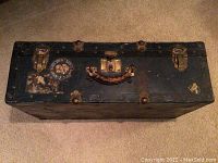 Top view of the vintage travel trunk showing the leather handle, metal hardware latches, and wear on the surface.
