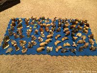 Wide angle photo showing a large assortment of Wade England ceramic figurines and miniatures arranged on a blue cloth, featuring numerous animal and character designs.