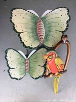 Front top view of the wooden butterfly wall shelf with attached parrot figurine showing the butterfly shelf surfaces and parrot handle