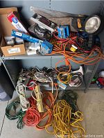 Shelf and floor view showing all lot contents including extension cords, power strips, hand saws, spotlight, electrical tape, and vacuum tubes