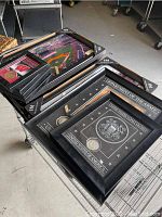 Stack of framed memorabilia on wire cart, showing different items with black frames and designs