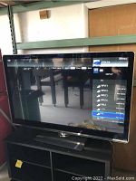 Front view of Sharp Aquos TV showing input menu on screen, placed on black stand.