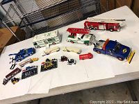 Full lot view showing all toy vehicles arranged on table including Hess trucks, fire trucks, forklifts, and construction vehicles.