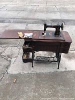 Full view of the King Rotary sewing machine set in its wooden table and cast iron foot pedal base with some sewing accessories on top, as well as open drawers showing more sewing materials.