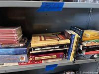 Shelf of books featuring a stack including Stickley Style, Builder's Comprehensive Dictionary, History of the United States, and Monopoly game box.