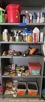Shelf with assorted cleaning chemicals, sprays, tapes, tools including battery powered drills, soldering tool, red bucket, and hardware items.