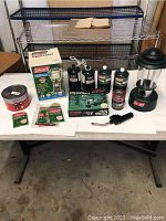 Front view of the lot showing unboxed propane lantern, propane fuel canisters, propane stove box, Sterno cans, and lantern accessories on a white table.