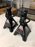 Pair of Craftsman 3 ton jack stands shown from front angle on white surface with metal shelving in background.
