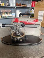 Full view of the David White surveyors leveling instrument mounted on its black base with carrying case behind it showing wear and red paint marks.