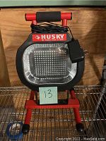 Front view of Husky LED work light showing LED panel, brand logo, and power cord wrapped around handle.