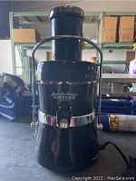 Front view showing the brand and model name on the body of the black juicer with chrome accent and top chute.