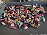 Wide shot of a large quantity of mixed nail polish bottles scattered in a tray, showing the diversity of colors and brands.