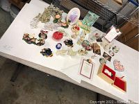 Wide view of table with multiple glass and porcelain collectibles showing figurines, plaques, and decorative items.