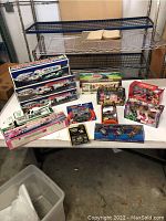 Overview of lot showing various boxed and loose toy vehicles on a table including Hess toy trucks and collectible sets