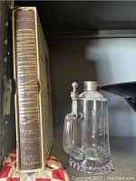Book titled 'Character Sketches Volume One' and clear glass beer stein with pewter lid on a shelf.
