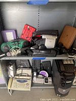 Photo showing top shelf with old boom box, projector, camera flashes, and other miscellaneous electronic items.
