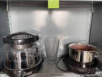 Shelf display with black Nuwave Pro Infrared Oven, clear glass chamber, large crystal vase, induction cooktop with stock pot.