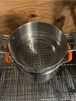 Top view of double boiler with perforated insert inside, showing orange handles and stainless steel finish.