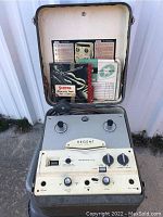 Photo of Regent Webcor reel to reel machine in open case showing front control panel, knobs, switches, and carrying handle, with accessories in lid pocket.