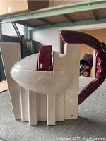 Front and side view of a ceramic teapot with modern geometric design, white body and burgundy handle and spout, San Marco signature visible.