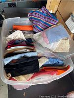 Plastic tote filled with assorted fabric remnants in various colors and patterns, visible folded and stacked inside.