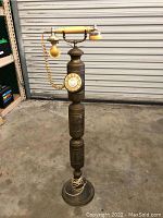 Front view of the vintage tall brass telephone showing the full height and rotary dial.