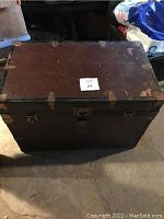 Closed old wooden chest showing worn surface, metal corner brackets, and latch mechanism on front.