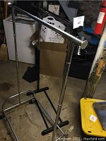 Adjustable metal portable wardrobe with stable base and some rust visible on the metal parts, located in basement setting with laundry items in background.