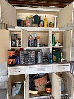 White multi-door storage cabinet with chemicals inside and various fluid containers on surface