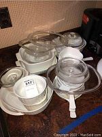 Overview of various Corning Ware bowls, roasting dishes, and glass lids arranged on countertop showing condition and quantity.