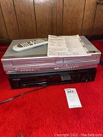 Top Sylvania DVD/CD player with built-in VCR, remote control and owner's manual on top, stacked on black Pioneer multi-call CD player with multiple CD trays.