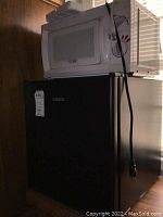 Photo showing the stacked configuration of the white Commercial Chef microwave on top of the black Galanz dorm refrigerator, highlighting brand labels and basic appliance features.