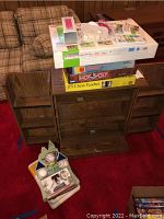 Lot shown on a red carpet in front of a plaid couch, with board games stacked on a wooden desk and two toy train car boxes and baseballs on the floor.