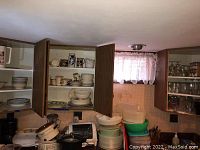 Open cabinet showing ceramic and porcelain bowls, plates, and tea cups stacked and arranged on shelves