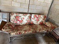 Full view of vintage metal glider with floral cushions showing seat, backrest, and armrests in a light floral print fabric.