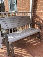 Front angle view of the plastic and metal gliding bench on an outdoor deck, showing seat, backrest, armrests, and metal gliding frame.