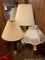 Four lamps together, showing variation in bases and shades, including two matching floral fabric shade lamps and one bronze base lamp with beige pleated shade.