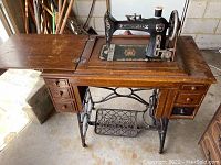 Full view of Minnesota Model H sewing machine mounted on a wooden sewing table with drawers and metal treadle base, showing overall condition and table details.
