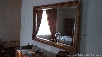 Full view of large rectangular wall mirror hanging above a dresser, reflecting window with curtains and dining furniture.