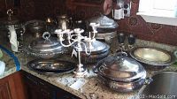 Overall view of multiple silverplate serving pieces including large lidded serving bowls, candelabra, and plates on countertop