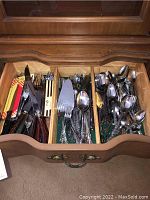 Drawer with organized silverware including forks, knives with colorful handles, spoons, and cake server, showing variety of utensils and handle patterns.