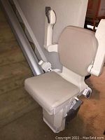 Beige stairlift seat mounted on straight aluminum rail on carpeted stairs