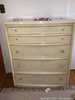 Front view of the vintage blonde finish tall dresser with five drawers and silver knobs, showing scratch marks and some wear.