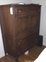 Right angled view of vintage tall dresser showing side panel, upper drawer, two cabinet doors in middle section, and two large lower drawers with carved detailing.