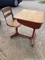 Full view of the vintage school desk with an attached chair showing wooden surfaces and reddish-brown metal frame, visible scratches and wear on wood and paint.