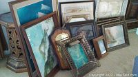 Photo showing various framed wall art pieces leaning against furniture including beach and sailing art and ornate frames.